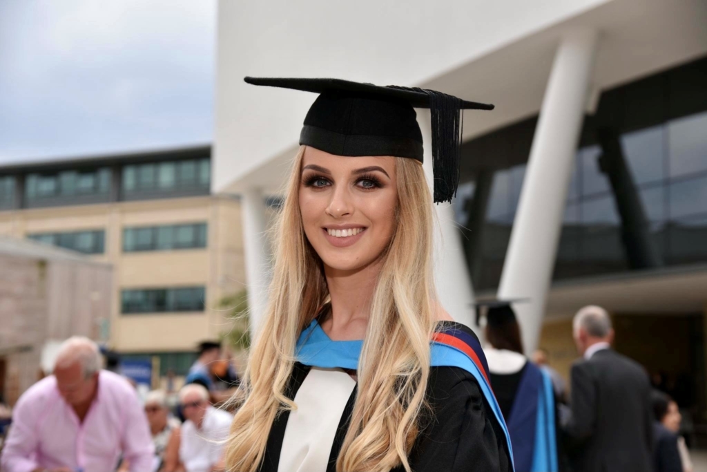 Photograph of Leah Etheridge at her graduation from the University of Huddersfield. She wears a graduation cap and cape.