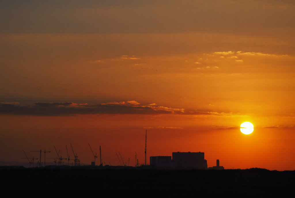 A photograph of the sun setting behind nuclear reactors at Hinkley Point A and B, with Hinkley Point C also under construction. 