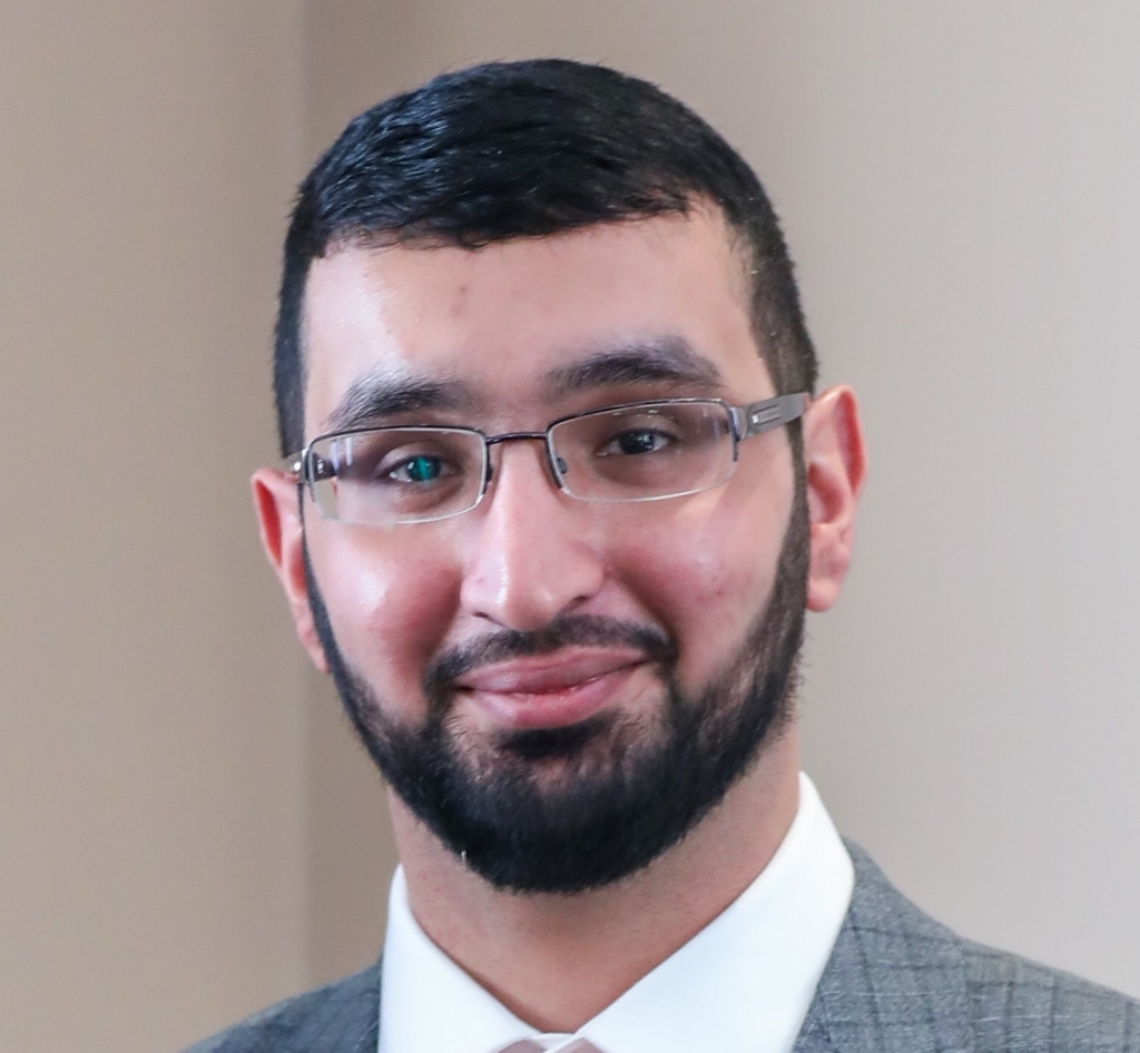 Photograph of AFCP researcher Akeel Ahmed. He is wearing glasses and a suit and looking into the camera, smiling. 