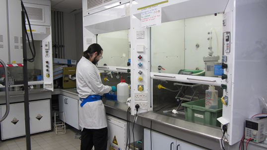 A photo of Ben Day, one of AFCP's early career workers, performing research to optimise the process. He is wearing a white lab coat, standing with his back turned to the camera as he works on an experiment at the bench. 